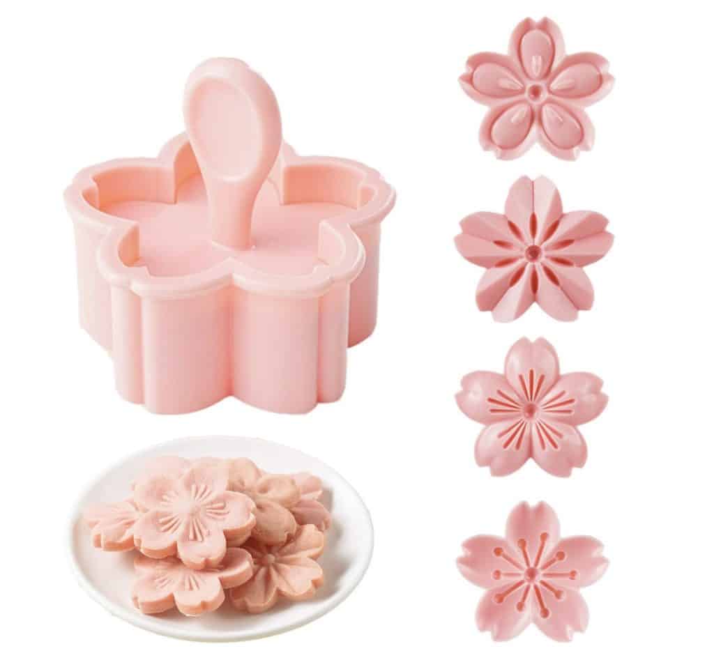A pink flower-shaped cookie cutter with a handle is shown next to four pink floral molds and a plate of pink flower-shaped cookies, perfect for creating my favorite floral desserts.